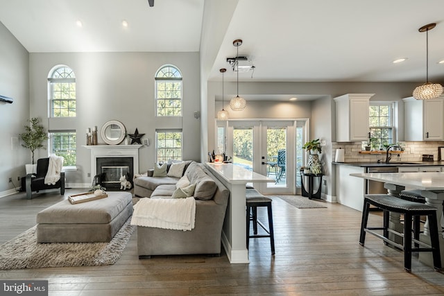 living area with dark wood-type flooring, a glass covered fireplace, french doors, a high ceiling, and baseboards