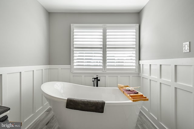 full bath featuring a freestanding tub, a decorative wall, wood finished floors, and wainscoting