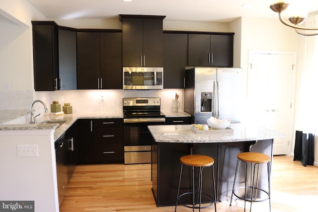 kitchen with appliances with stainless steel finishes, light wood-type flooring, a kitchen breakfast bar, and a sink