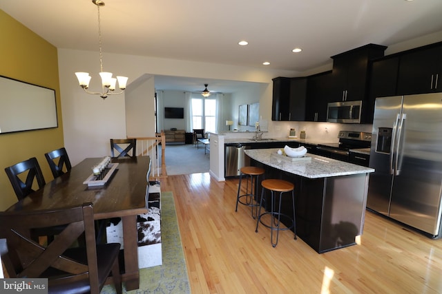 kitchen featuring light wood-style flooring, a sink, stainless steel appliances, a kitchen bar, and dark cabinets