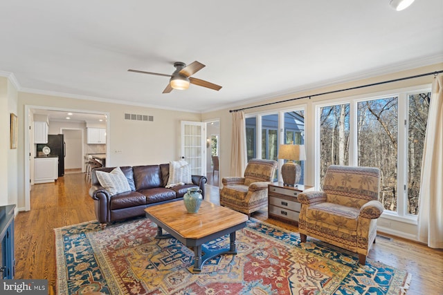 living area featuring light wood-style floors, a healthy amount of sunlight, ornamental molding, and a ceiling fan