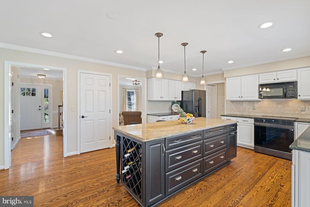 kitchen with wood finished floors, a kitchen island, black appliances, white cabinets, and crown molding