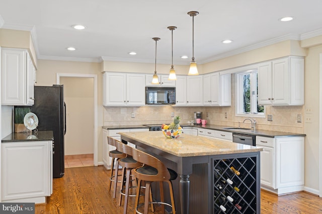 kitchen with a kitchen island, black appliances, wood finished floors, and white cabinetry