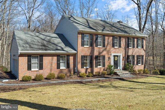 colonial home with brick siding, a chimney, and a front yard