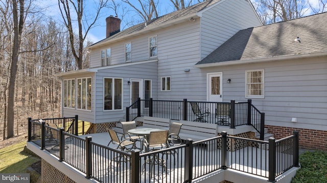 back of property with outdoor dining space, roof with shingles, a sunroom, a wooden deck, and a chimney