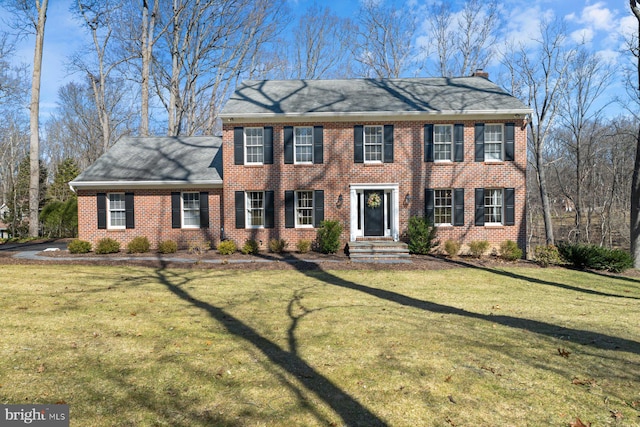 colonial-style house with brick siding, a chimney, and a front lawn