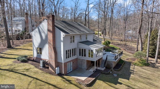 view of side of home featuring stairs, a lawn, a chimney, a deck, and driveway