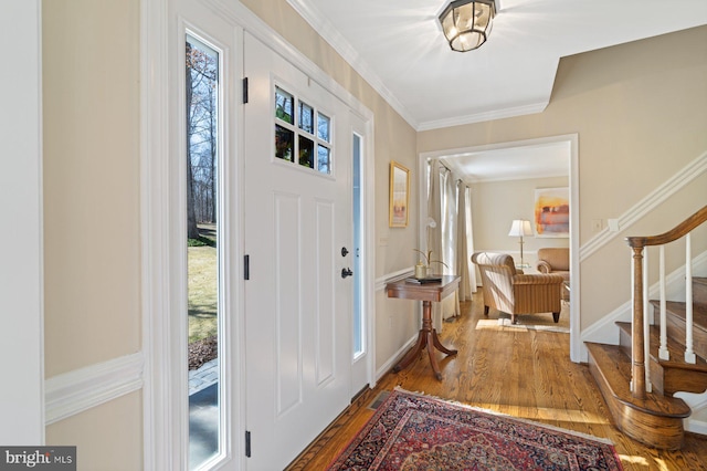 entrance foyer with baseboards, wood finished floors, ornamental molding, and stairs