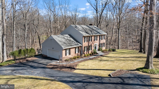 view of front of house featuring brick siding, a wooded view, a front yard, a garage, and driveway