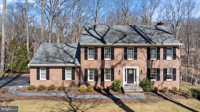 colonial inspired home with brick siding and a chimney