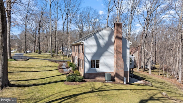 view of side of home with central AC unit, a lawn, and a chimney