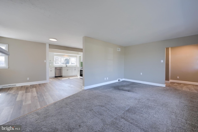 unfurnished living room featuring a sink, visible vents, baseboards, and light colored carpet