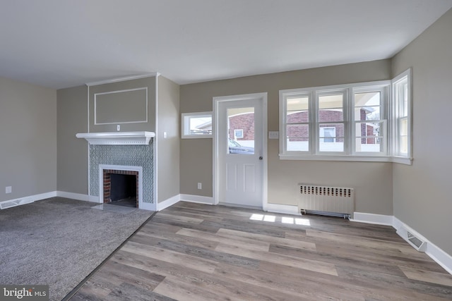 unfurnished living room with a tiled fireplace, visible vents, radiator, and baseboards