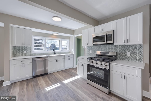 kitchen featuring light wood finished floors, a sink, stainless steel appliances, light countertops, and white cabinets