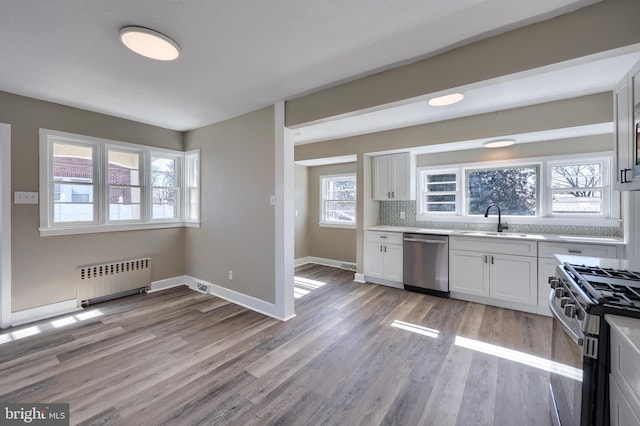 kitchen with light wood finished floors, backsplash, radiator, appliances with stainless steel finishes, and a sink