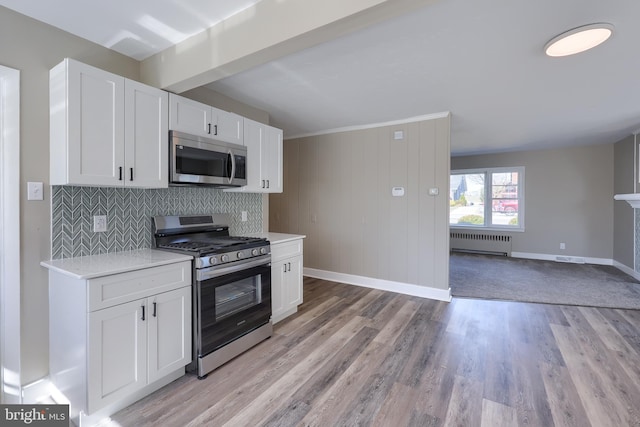 kitchen with backsplash, radiator heating unit, white cabinetry, stainless steel appliances, and light countertops