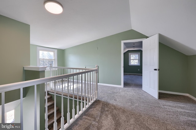 hallway with lofted ceiling, an upstairs landing, baseboards, and carpet floors