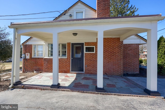 view of exterior entry with brick siding and a chimney