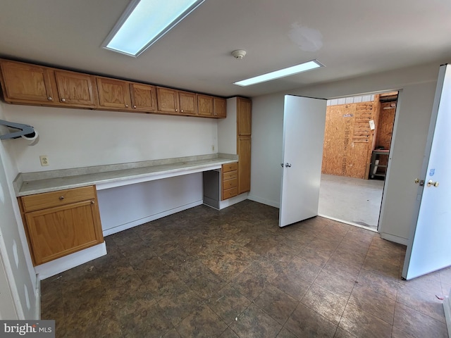 kitchen featuring brown cabinets, built in study area, light countertops, and baseboards