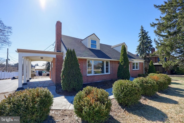 view of home's exterior with fence, roof with shingles, a chimney, a carport, and brick siding