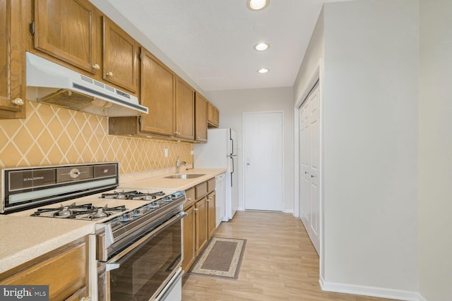 kitchen with white appliances, a sink, light countertops, under cabinet range hood, and backsplash