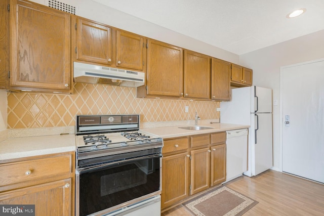 kitchen with white appliances, a sink, light countertops, under cabinet range hood, and tasteful backsplash