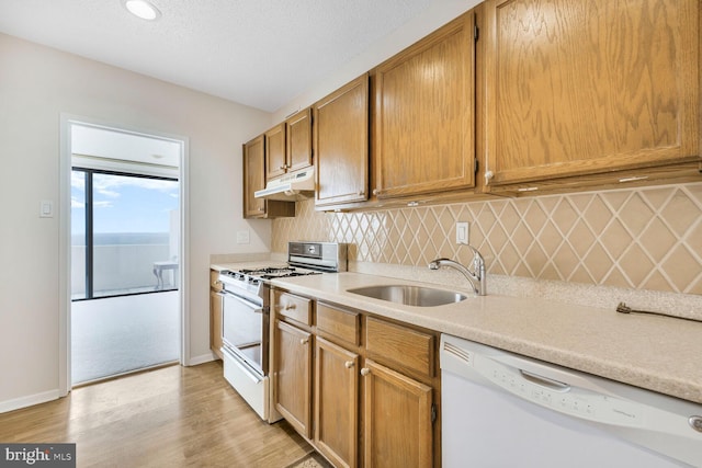 kitchen with tasteful backsplash, under cabinet range hood, light countertops, white appliances, and a sink