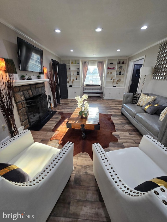 living room with wood finished floors, crown molding, a stone fireplace, built in shelves, and recessed lighting