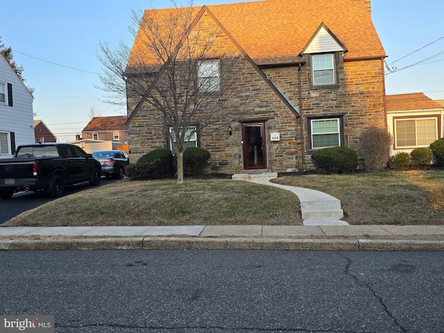 view of front of house with stone siding, a shingled roof, and a front lawn