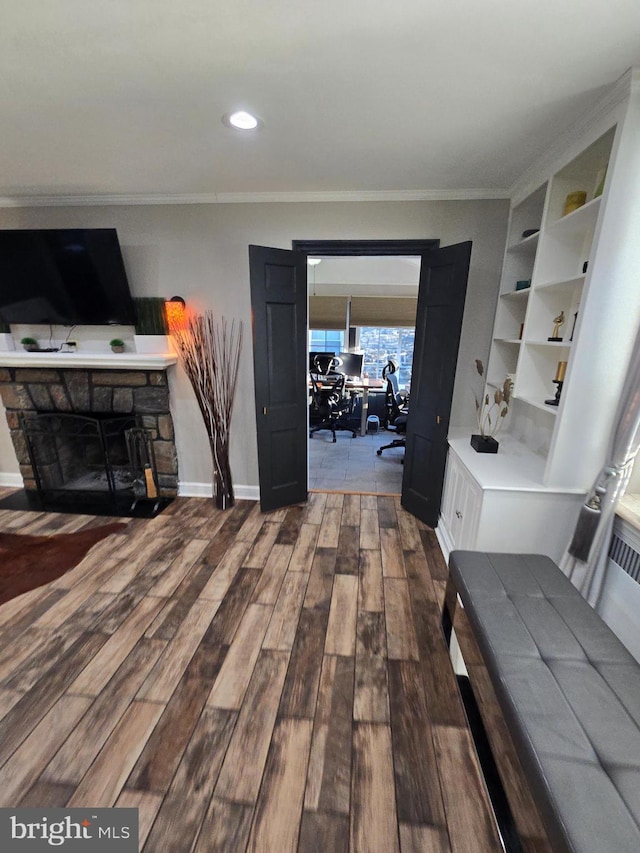 interior space with baseboards, wood finished floors, crown molding, a stone fireplace, and recessed lighting