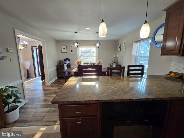 kitchen with oven, a peninsula, dark wood-type flooring, dark stone countertops, and pendant lighting