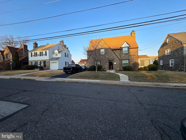 view of front of home with stone siding, aphalt driveway, a chimney, and a front yard