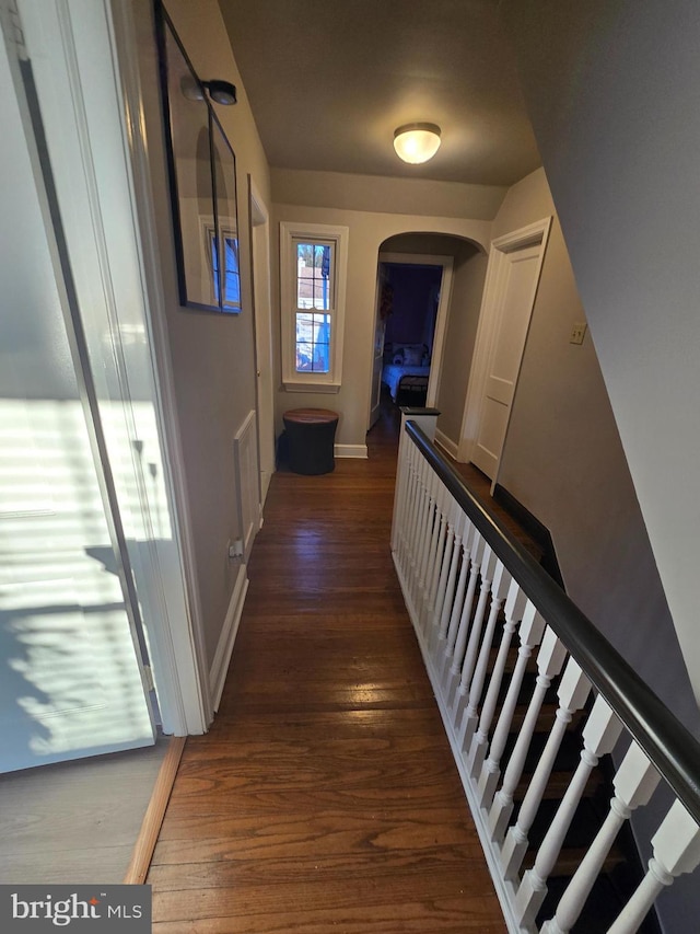 hallway featuring stairway, baseboards, arched walkways, and wood finished floors