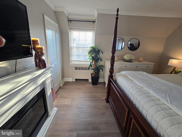 bedroom featuring baseboards, radiator heating unit, wood finished floors, crown molding, and a fireplace