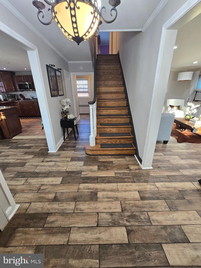 staircase with ornamental molding, a notable chandelier, baseboards, and wood finished floors