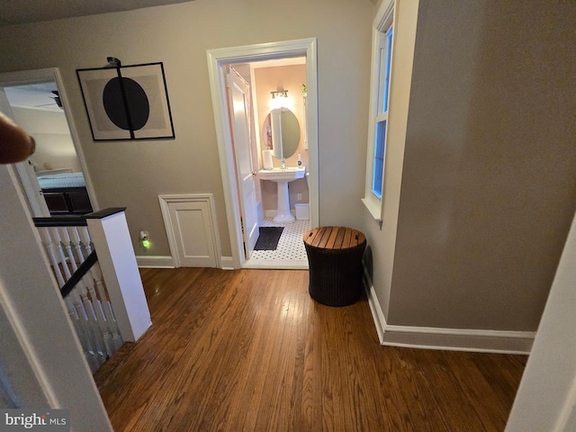 hallway featuring a sink, wood finished floors, an upstairs landing, and baseboards