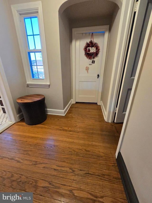 hallway featuring dark wood-type flooring, arched walkways, and baseboards