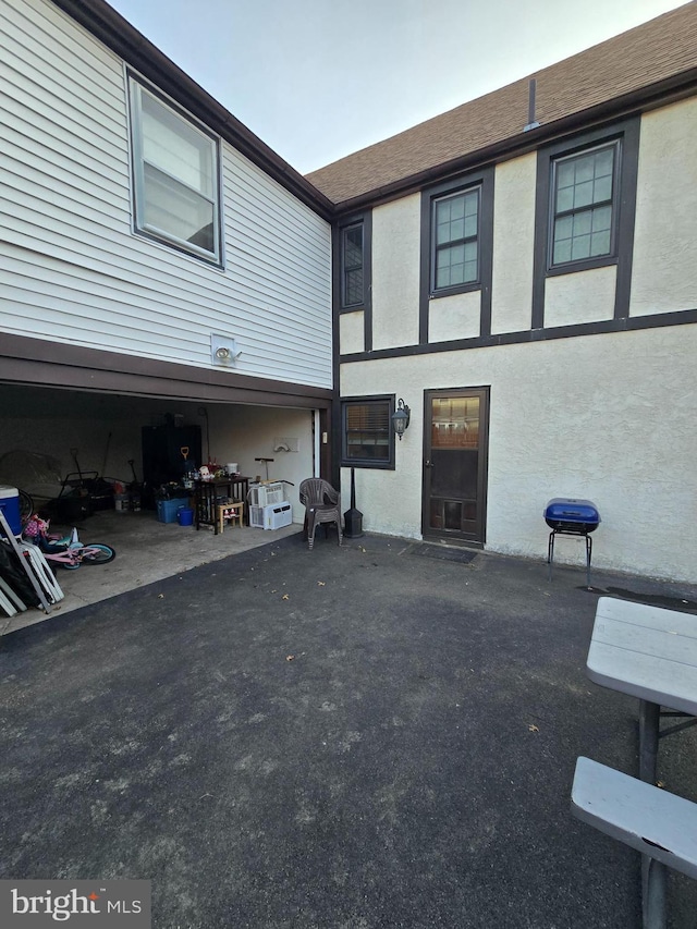 rear view of house with a shingled roof and stucco siding