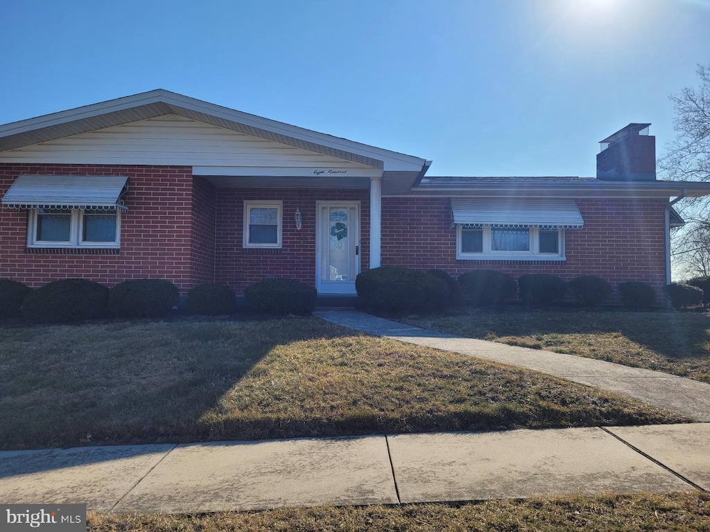 view of front of house with brick siding, a chimney, and a front lawn