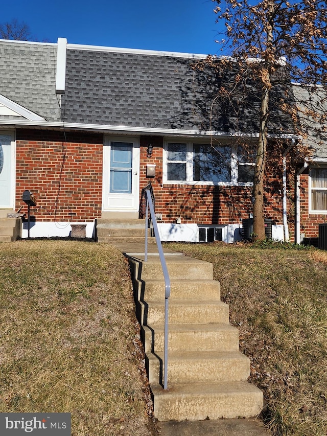 view of front facade featuring a shingled roof, entry steps, brick siding, and mansard roof