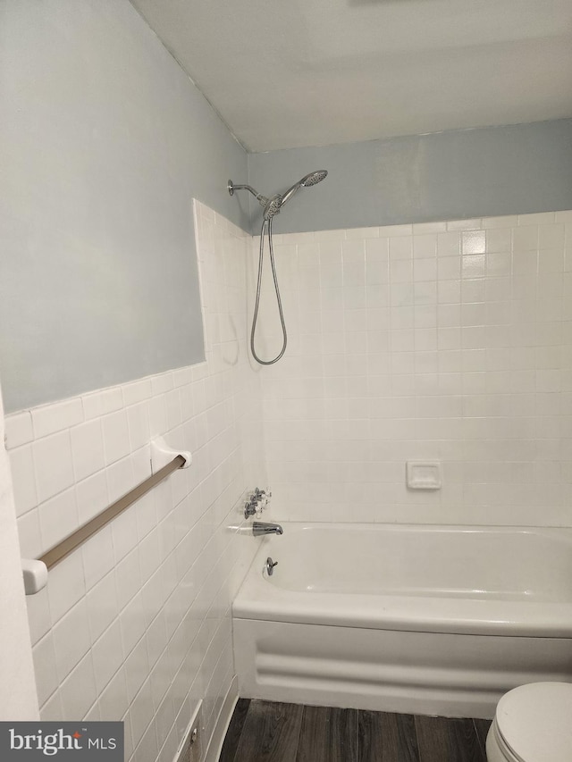 full bath featuring shower / bath combination, toilet, a wainscoted wall, wood finished floors, and tile walls