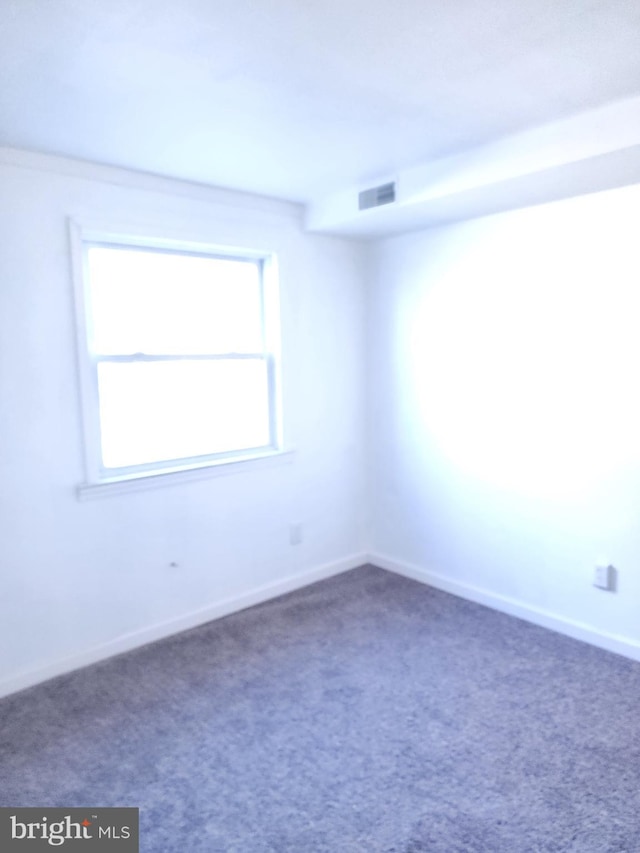 unfurnished room with carpet floors, visible vents, and baseboards