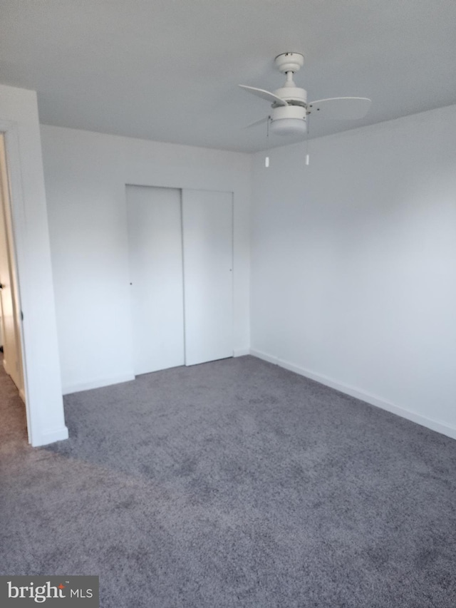 unfurnished bedroom with a ceiling fan, dark colored carpet, and a closet