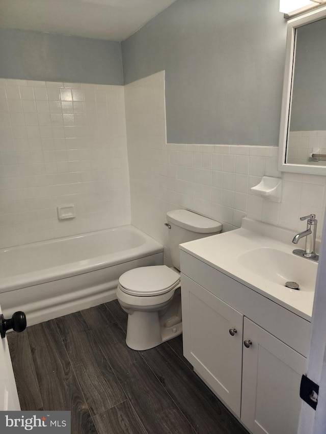 bathroom featuring toilet, a wainscoted wall, wood finished floors, vanity, and tile walls