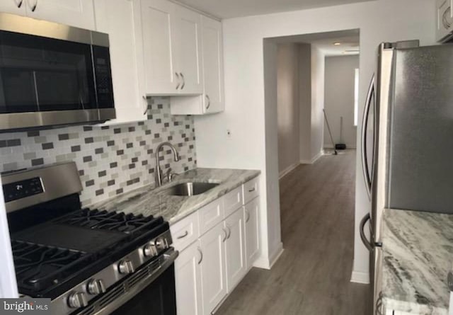 kitchen with appliances with stainless steel finishes, light stone counters, wood finished floors, white cabinetry, and a sink