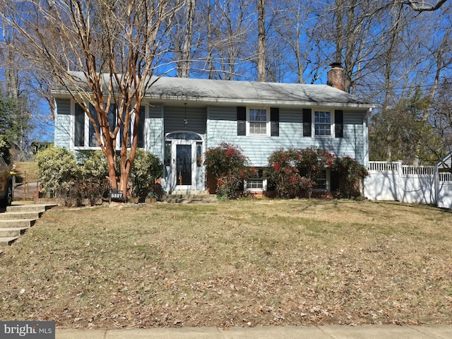 split foyer home with a chimney, fence, and a front lawn