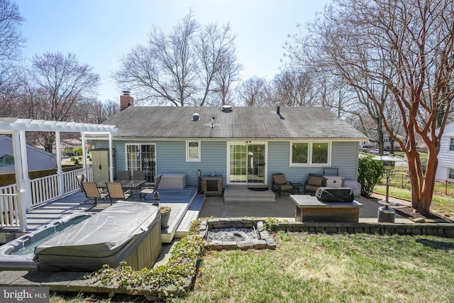 back of house featuring a wooden deck, an outdoor fire pit, a pergola, a chimney, and a hot tub