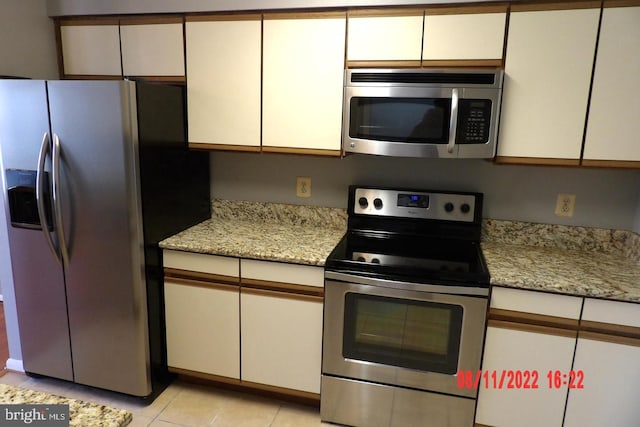 kitchen featuring appliances with stainless steel finishes, light stone countertops, white cabinetry, and light tile patterned floors