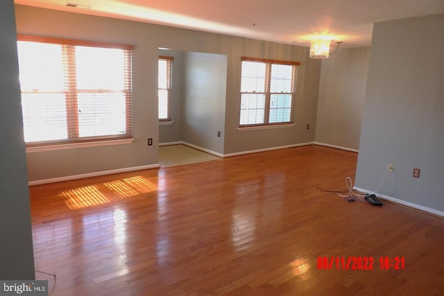 spare room featuring a chandelier, baseboards, and hardwood / wood-style flooring