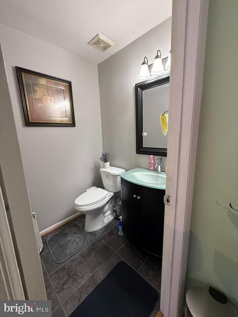 half bathroom featuring toilet, baseboards, visible vents, and vanity